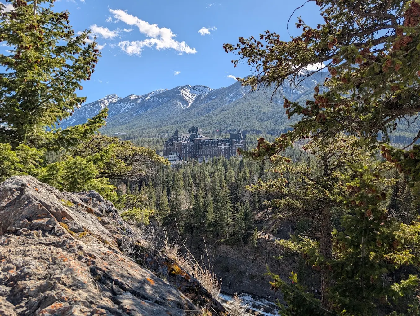 Rock outcrop framed by pine branches with the Fairmont Banff Springs visible in the distance