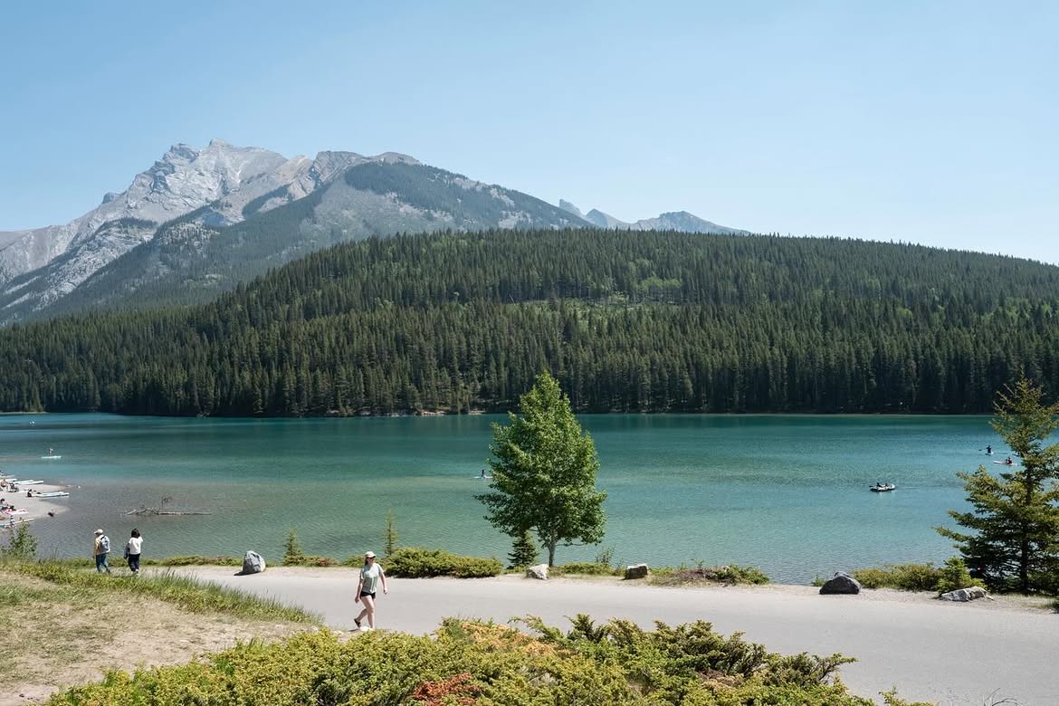 Visitors walking the shoreline path at Two Jack Lake with mountains and turquoise water in the background