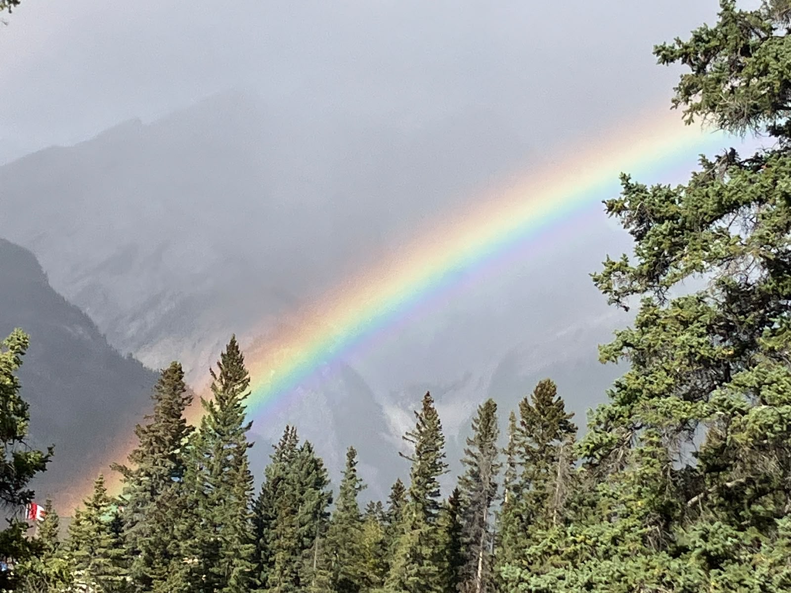 Rainbow over misty mountains and evergreens above the town of Banff