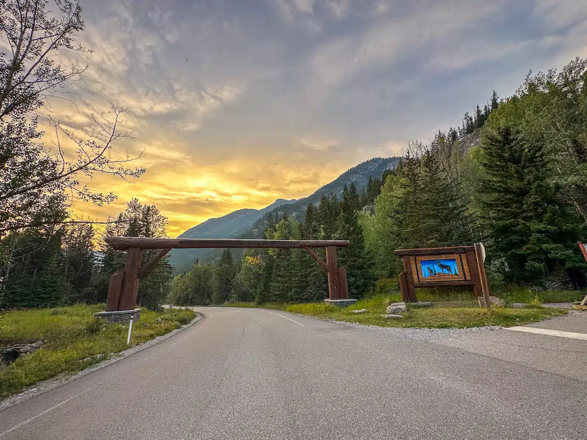 Log entrance arch and wildlife sign at the start of the Bow Valley Parkway, with forested mountains under a sunset sky