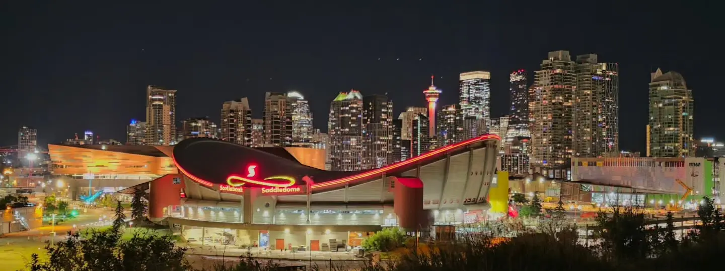 Scotiabank Saddledome lit at night in front of the Downtown Calgary skyline and Calgary Tower