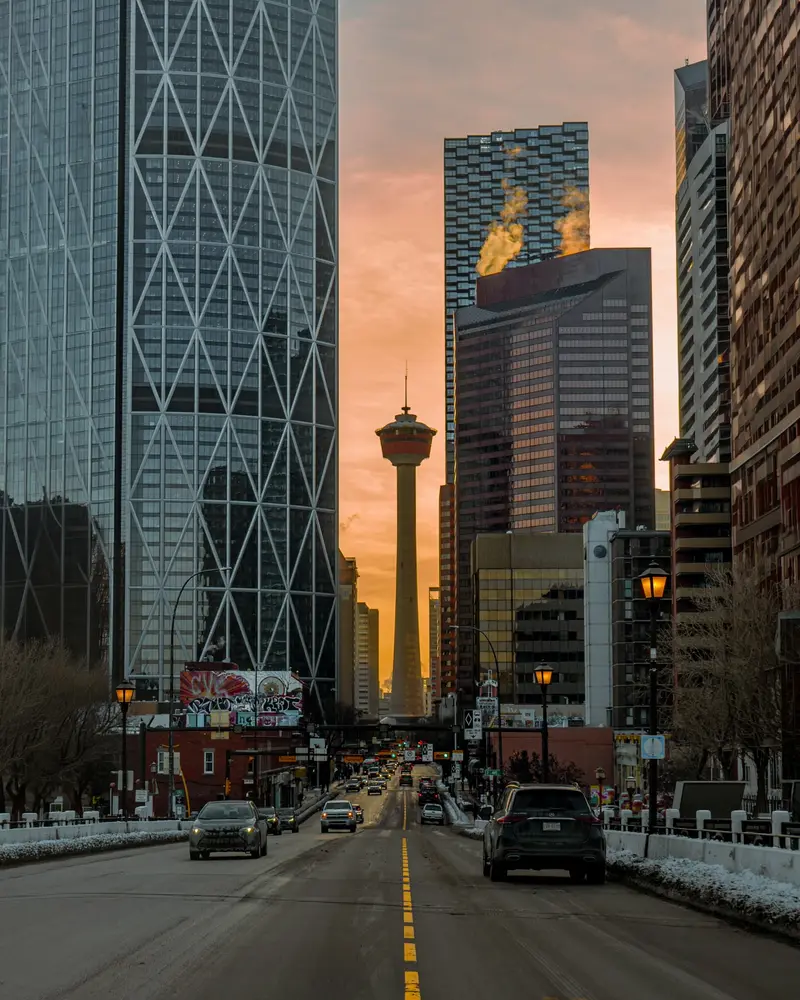 Traffic on a snowy Downtown Calgary street at sunrise, with Calgary Tower framed between office towers