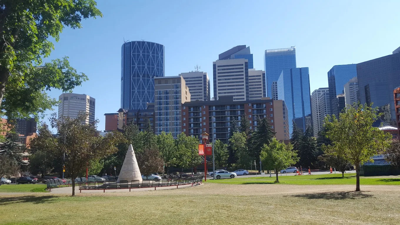 Downtown Calgary towers seen from a green park with benches and mature trees