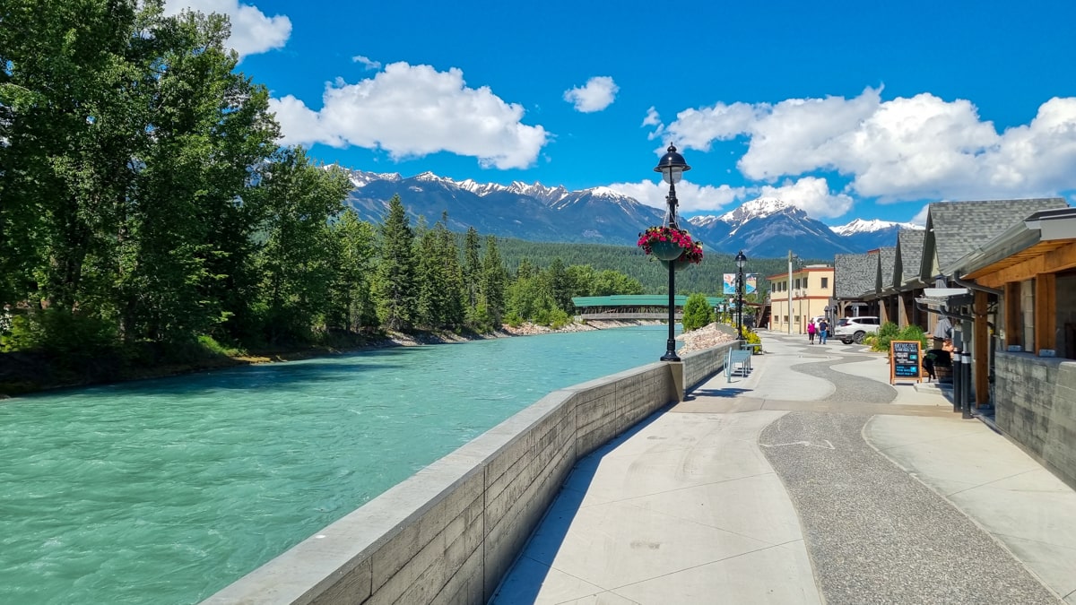 Riverfront boardwalk in downtown Golden, BC beside the turquoise Kicking Horse River, with mountains on the skyline