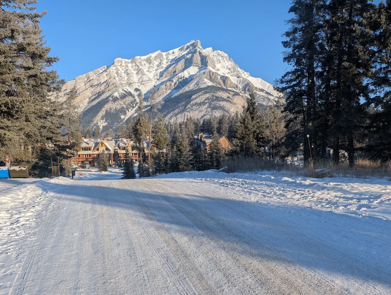 Snowy road leading toward Hidden Ridge Resort with Cascade Mountain in view, Banff