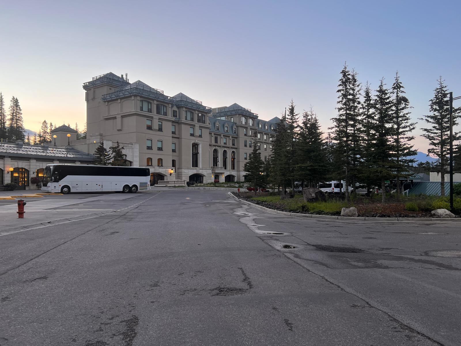 Fairmont Chateau Lake Louise at dusk with evergreen trees and a coach in the forecourt
