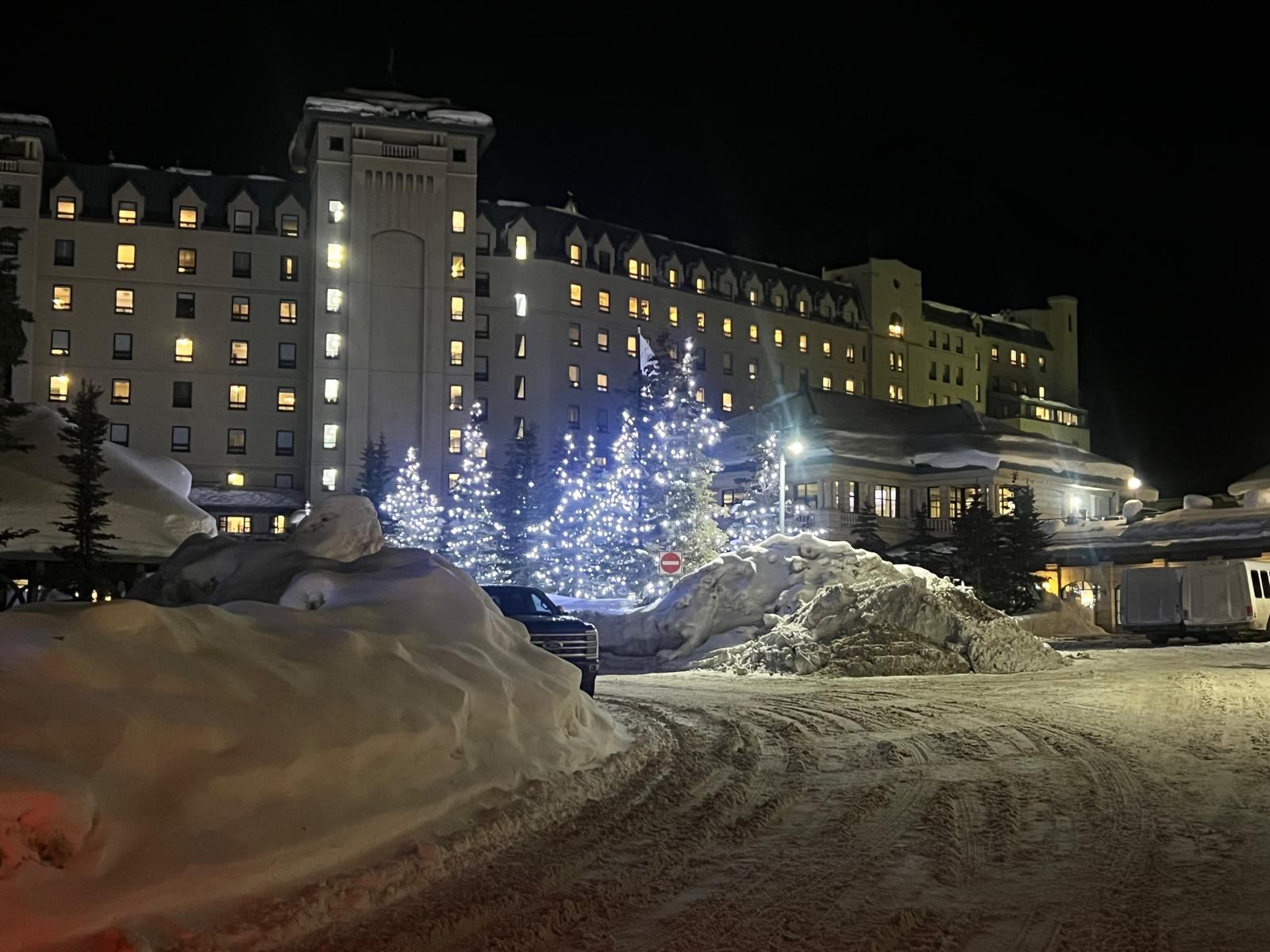 Fairmont Chateau Lake Louise at night in winter, with snowbanks and trees wrapped in blue lights
