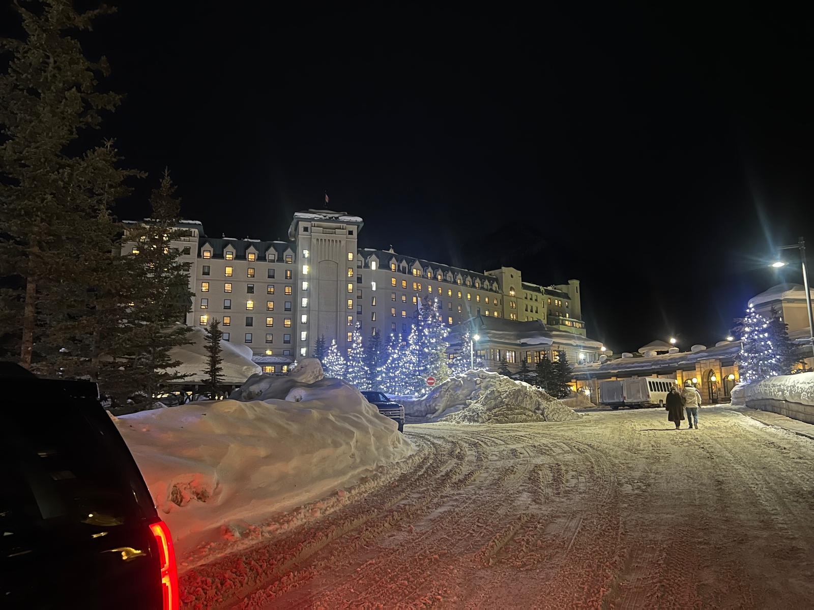 Fairmont Chateau Lake Louise lit up on a winter night, with snowbanks and lit trees along the drive