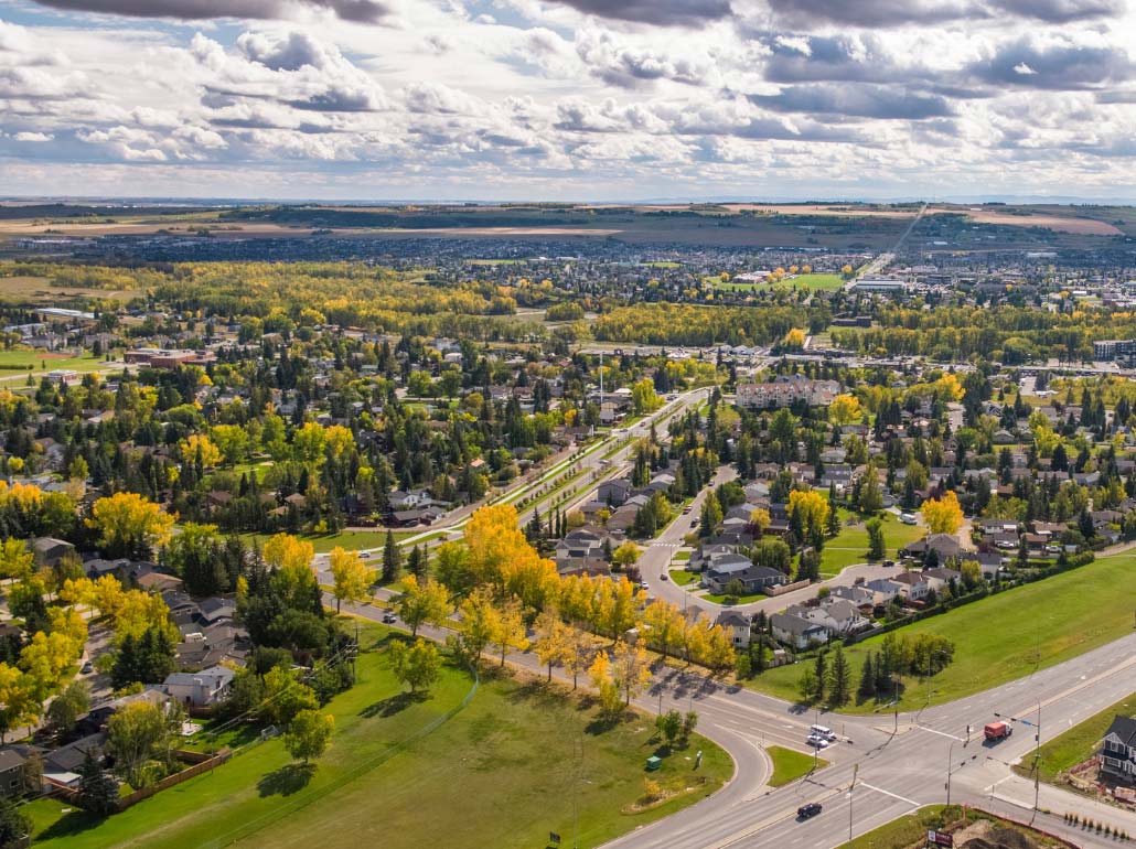 Aerial view of Okotoks in autumn, with tree-lined neighbourhoods and the roads leading out toward Highway 2