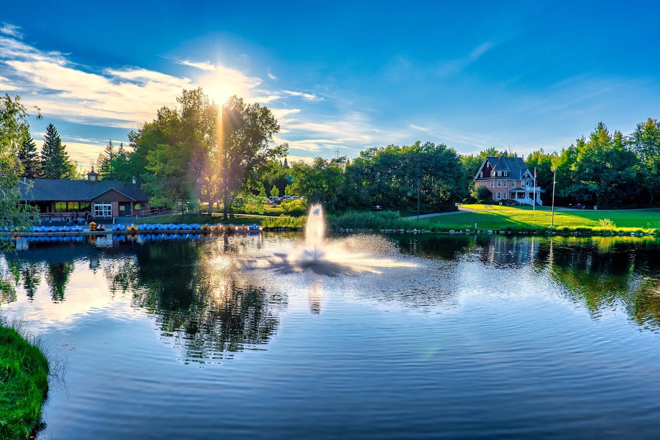 Evening sun over a Red Deer park pond with a fountain and moored paddle boats