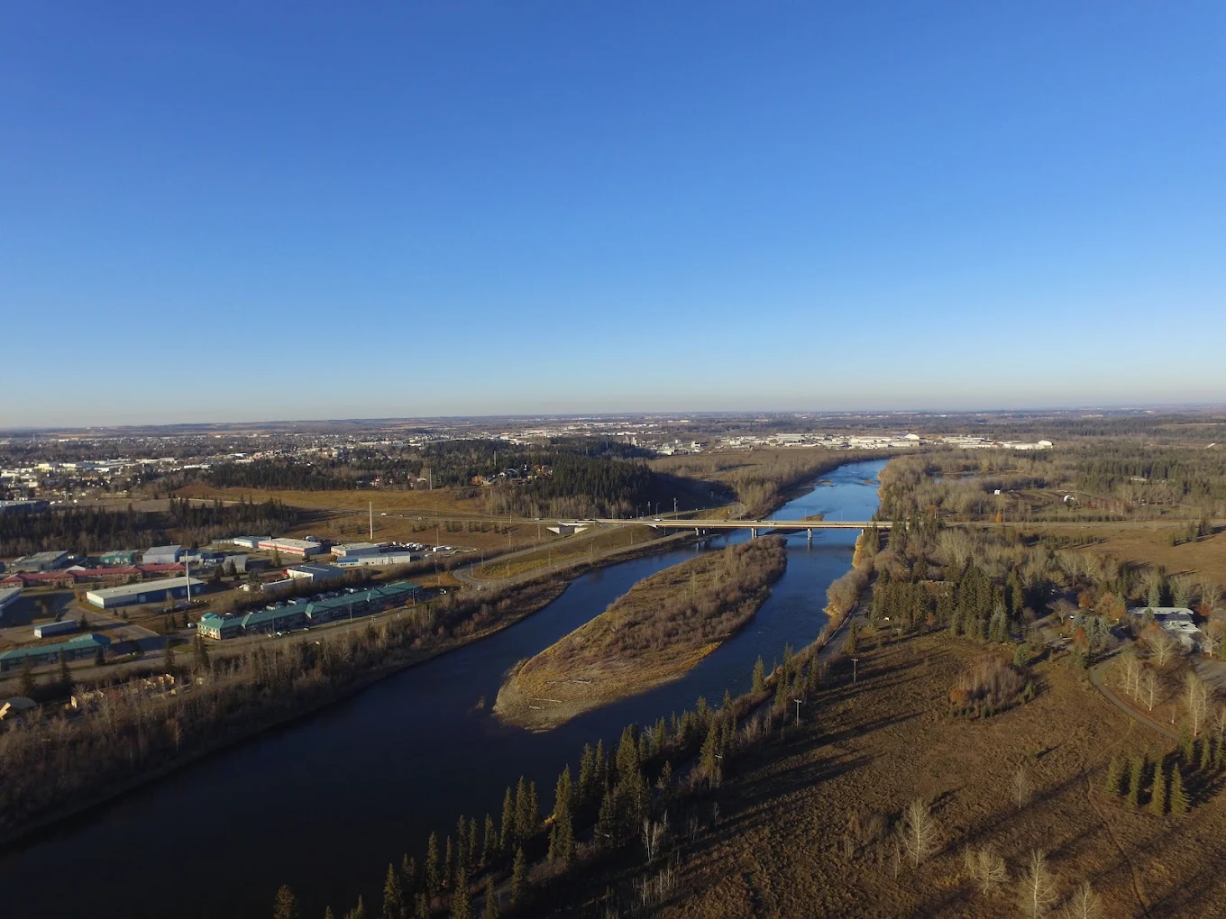 Aerial view of the Red Deer River winding past the city and its highway bridge